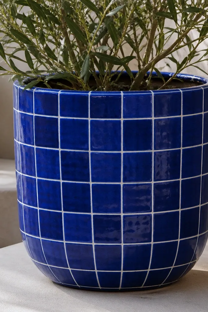 A pot painted cobalt blue with a grid of white lines forming tile squares. The grid wraps around the pot and some squares are slightly offset for a handmade tile look.