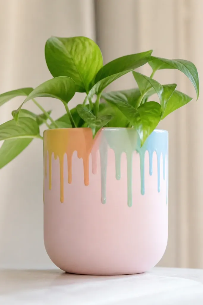 A pot with a pastel base in pale pink and a rainbow drip border across the top edge. The drips hang down in thin lines of yellow, orange, mint, and light blue.