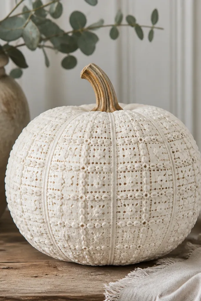 A white pumpkin with a grid of small raised dots and short lines, like a crocheted doily pattern. The surface looks matte and tactile.