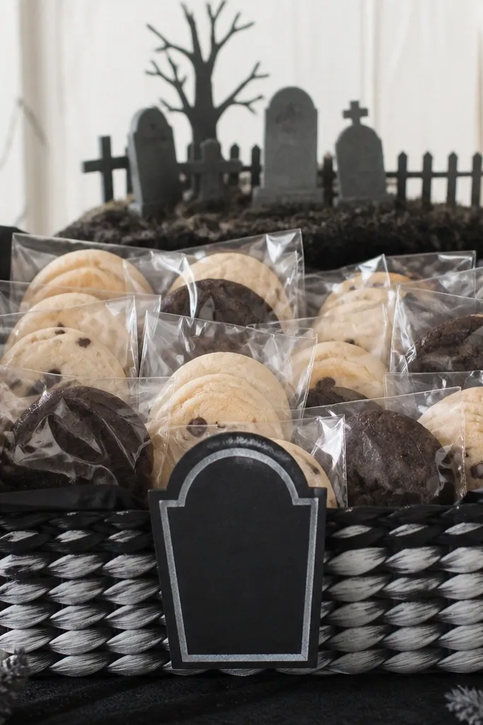 A black-and-white paper themed basket with a tombstone-shaped tag in the front, black tissue lining, and neatly packed cookies in clear bags. A small faux graveyard sign sits at the top.