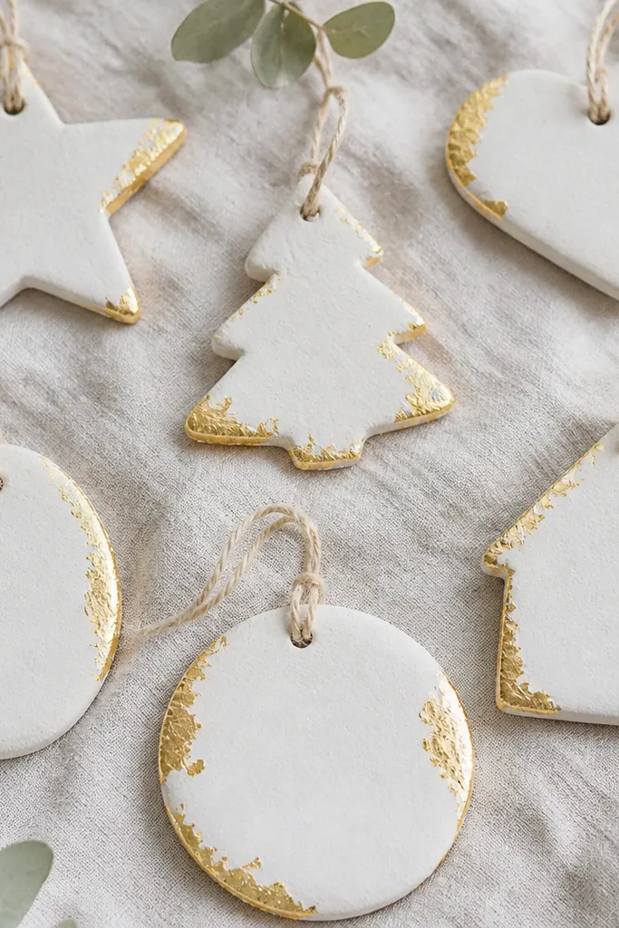 Salt dough ornaments painted soft white with small torn pieces of gold leaf pressed on the edges. The gold catches light in irregular patches.