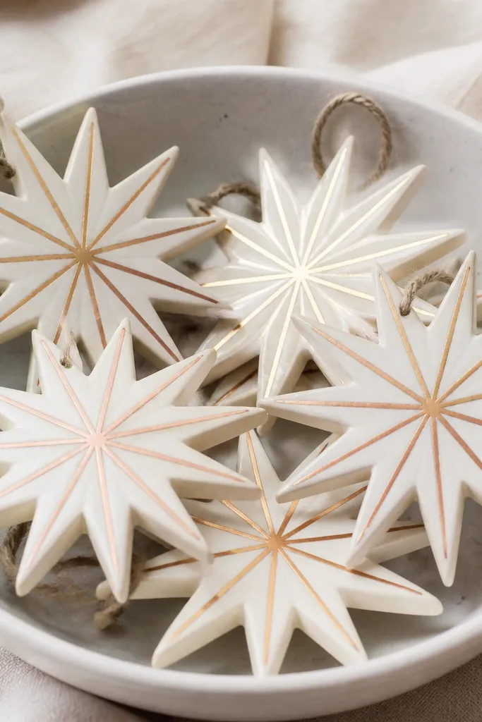 Starburst-shaped ornaments painted off-white with thin metallic gold and copper stripes radiating from the center. The rays look evenly spaced.