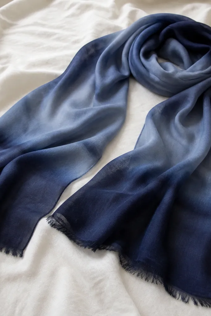 A long scarf laid on a light sheet. It shows a smooth navy-to-slate gradient with darker ends and lighter middle, plus visible dye pooling that still looks controlled. The fabric is soft and slightly drapey.