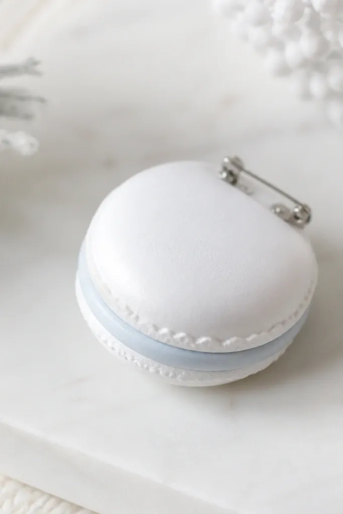 A winter white macaron-shaped paper squishy pin with a pastel filling layer. It has a rounded top and a slightly padded center, with a small pin back attached.