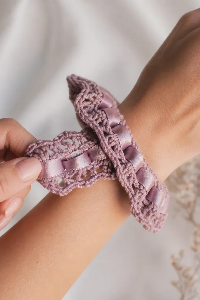 A crochet scrunchie with a satin ribbon stitched into the center, shown on a wrist and stretched slightly.