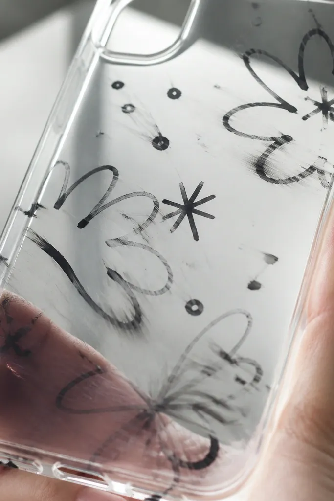A clear case with a hand-drawn design in black marker that looks partially smeared. A close-up shows blurred lines where alcohol touched the surface.