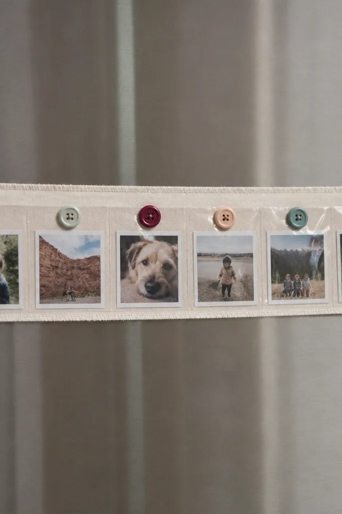 A horizontal strip of fabric with small printed photo squares behind clear tape. Each photo is topped with a flat button and small magnets hold the strip to a metal surface.