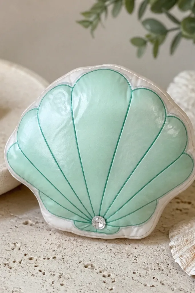 A seashell-shaped paper squishy with a seafoam green body and a pearly off-white edge. The ridges are drawn as curved lines, and the shell has a tiny gem-like dot in the center.