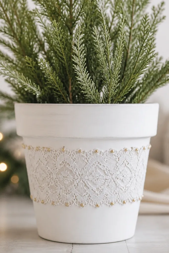 A pot with a painted white base and a lace band wrapped around the middle. The lace has tiny dots of gold paint at the edges for a delicate, holiday-style look.