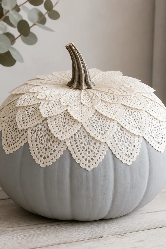 A pumpkin covered at the top with a sunburst pattern made from layered paper doily petals. The doily pieces are cream and slightly translucent. The rest of the pumpkin is painted a pale gray, and the edges look smooth where paper meets paint.