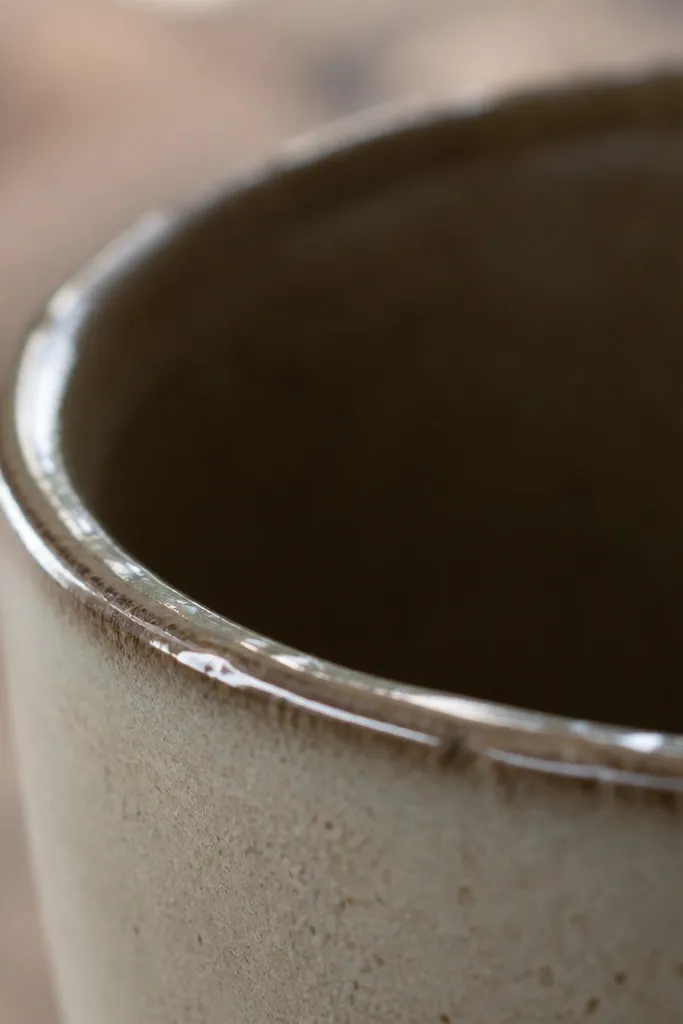 A close-up photo of a mug rim. The glaze is glossy on top, but the inner lip edge looks slightly raised with tiny ridges. The rim catches light in uneven lines.