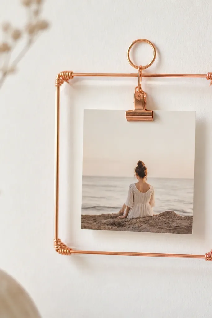 A mini photo frame made from rose gold wire, with a small photo clipped in the center. The wire is wrapped tightly around corners and has a clean, rounded loop at the top for hanging.