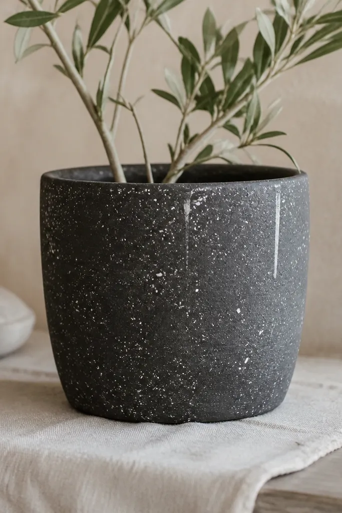 A charcoal-gray pot covered in scattered white speckles and a few short, controlled paint drips; the rim is charcoal and the surface looks intentionally matte and textured.