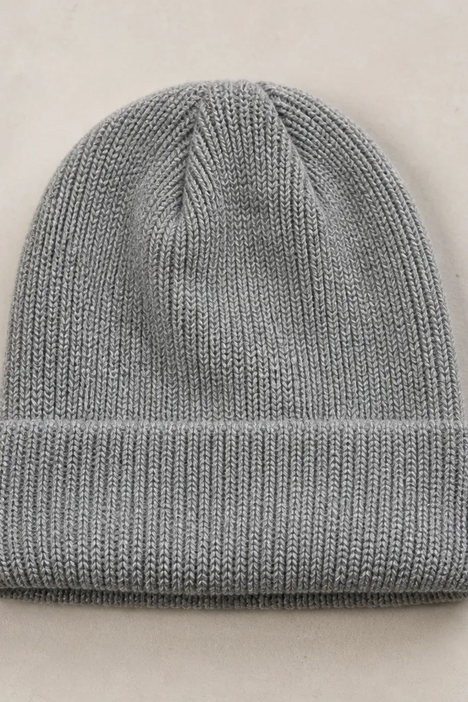A simple knit beanie in heather gray with a folded cuff and no pom. The knit texture is visible, and the hat sits flat on a neutral surface.
