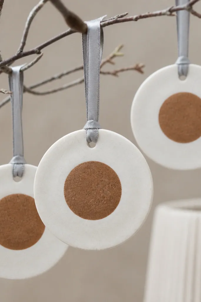 Round discs with a pale, chalky snowy white outer area and a darker cinnamon center circle. The look is two-tone and matte. The discs hang from light gray ribbon.