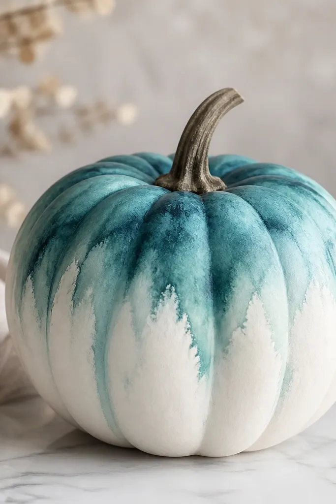 A white pumpkin with a teal watercolor wash that looks like it bleeds at the edges; darker teal pools near the top and fades down, with no hard lines.