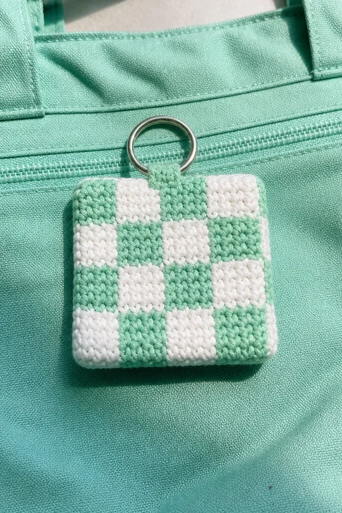 A small mint and white checkerboard crocheted charm with a side clip loop.