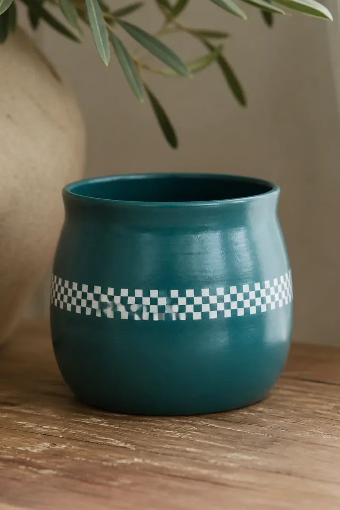 A small pot painted matte teal with a white checker band across the middle. The checks are tiny squares, and the band is straight and centered, with a clear coat that slightly glosses the teal.