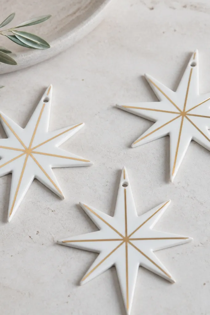Starburst ornaments with a crisp white base and gold leaf tape radiating from the center. The gold lines look like thin metallic strips, with clean points and a small hanging hole.