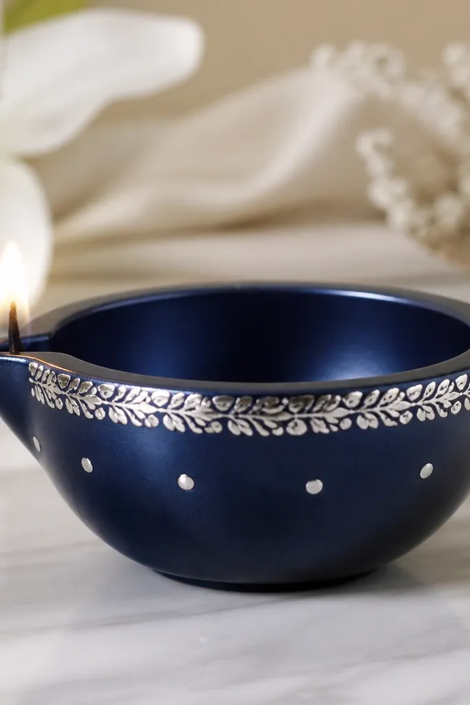 A deep navy diya with a silver foil leaf strip around the top rim and a few silver dot accents near the side. The finish looks metallic and clean.