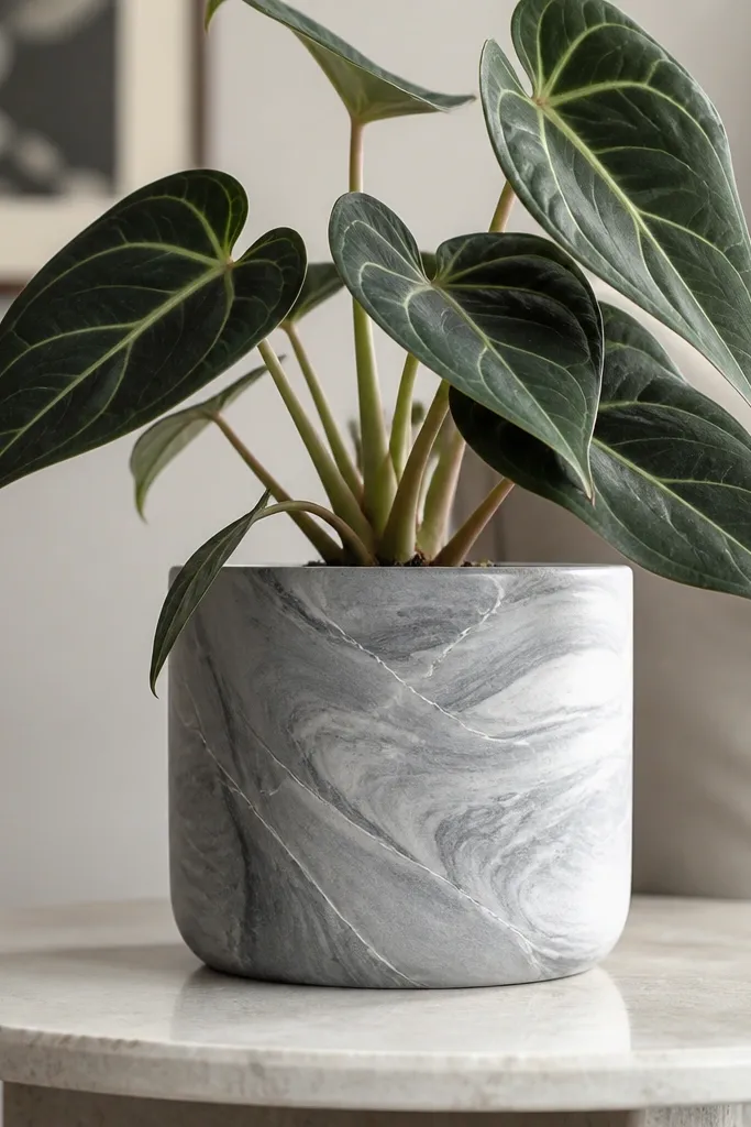 A small pot painted in light gray marble style with darker gray swirls and thin white vein lines. The finish is satin, and the plant leaves look dramatic against the pattern.