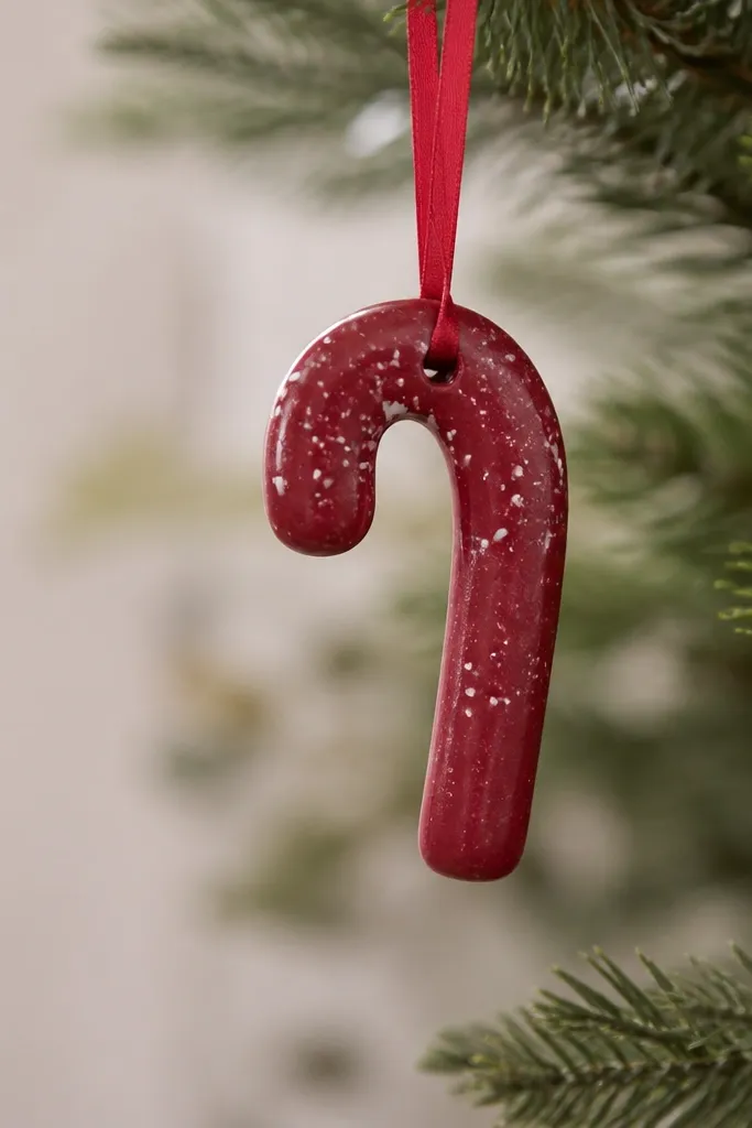 A small salt dough candy cane ornament painted deep cranberry red with tiny speckles of opaque white along the curve; it hangs from a thin red ribbon and has a smooth, lightly glossy finish.